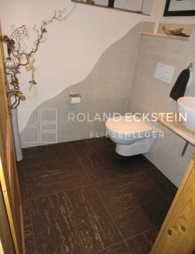 Klein, modernes Badezimmer mit Toilette und Waschbecken auf gefliester Fläche.