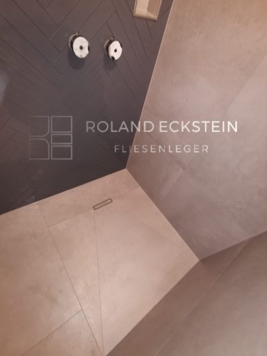 Moderne Dusche mit grauen Fliesen und zwei Armaturen, minimalistisches Design.