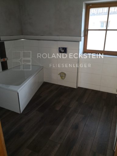Badezimmer mit hellen Fliesen, Holzfußboden und Fensterlicht.