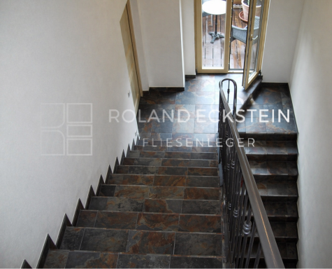 Treppenhaus mit steinernen Stufen und Zugang zu einem Balkon.