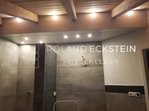 Moderne Badezimmeransicht mit Holzdeckenbalken und spotbeleuchteter Wand.