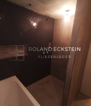 Moderne Dusche mit geschliffenen Fliesen und Holzregal in neutralen Farbtönen.
