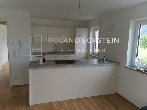 Moderne Küche mit Kochinsel, hellen Wänden und Holzfußboden. Fenster mit Blick ins Freie.