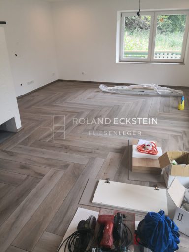 Leerer Raum mit Holzboden, Kartons und Baustellenmaterialien verteilt.