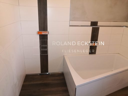 Moderne Badezimmeransicht mit Badewanne, Fliesen und Holzfußboden.